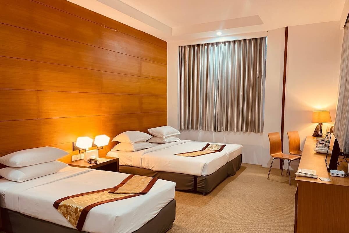 A hotel room with two beds, a desk with a computer, a chair, and a window with curtains.