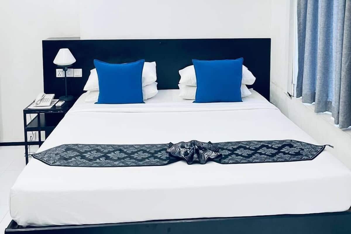A modern hotel room with a large bed, a bedside table with a lamp, and a power outlet.