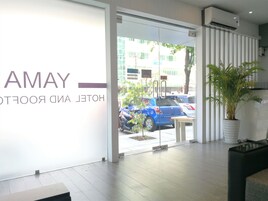 Entrada de un hotel con puerta de cristal, un cartel que dice "AMAY HOTEL ROOFTOP" y una planta en maceta a la derecha.