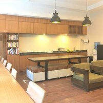 Una cocina moderna con armarios de madera, una larga mesa de comedor y dos lámparas colgantes.