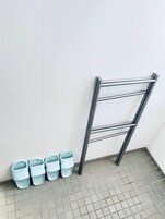 Una esquina con un estante metálico contra una pared blanca y suelo de baldosas.