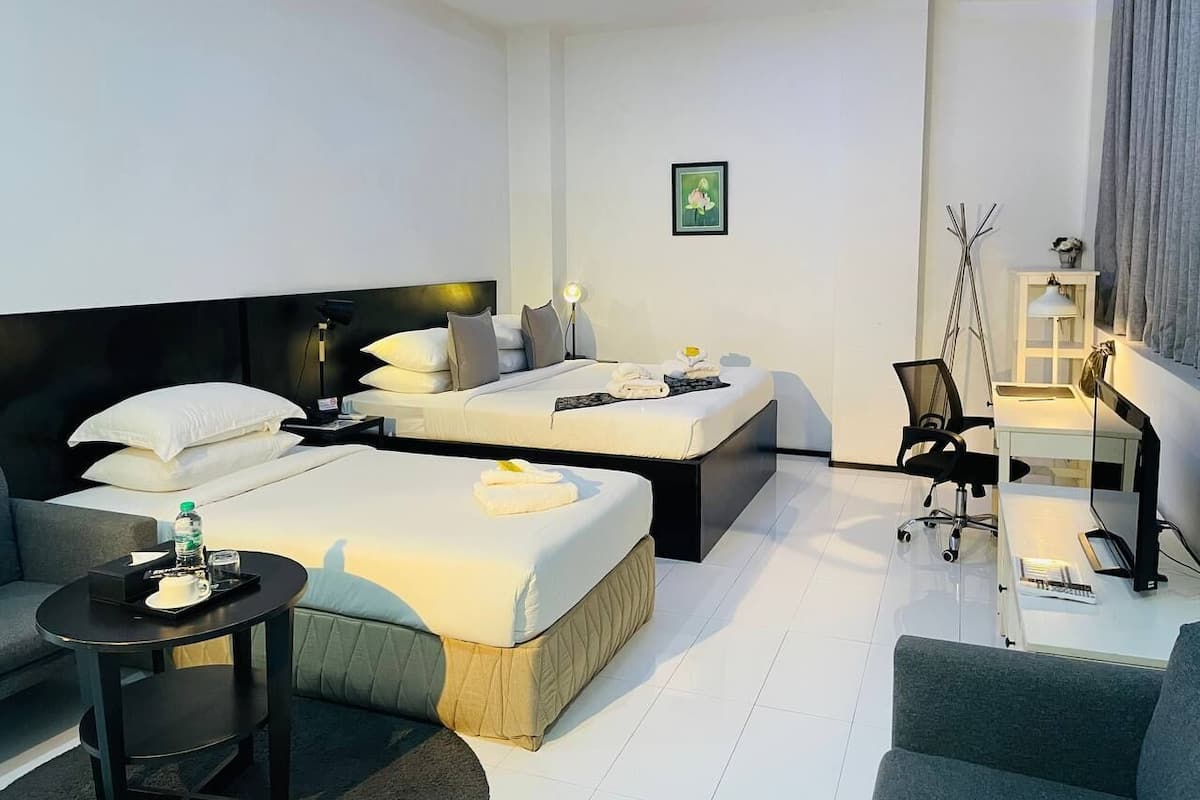 A modern hotel room with two beds, a desk, a chair, and a small table with amenities.