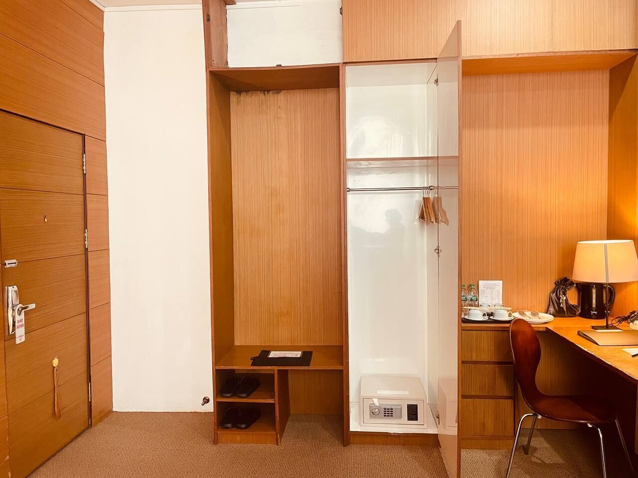 Una habitación de hotel compacta con un armario de madera, un escritorio pequeño con una lámpara y una silla.