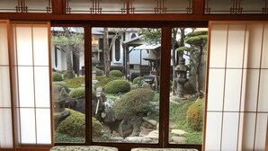 Ein traditioneller japanischer Raum mit Tatami-Boden, Shoji-Schirm und Blick auf einen Zen-Garten durch eine Schiebetür.