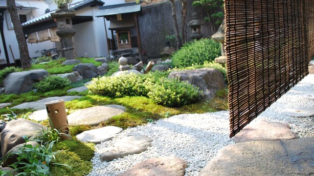 Ein traditioneller japanischer Garten mit Kieswegen, Moos und Steinen.