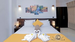 Une chambre d’hôtel avec un grand lit, une tête de lit dotée d’un luminaire, un mur orné de trois tableaux encadrés et une décoration artistique réalisée avec des serviettes sur le lit.