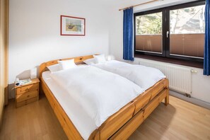 A room with a wooden bed, a nightstand, a window with blinds, and a framed picture on the wall.