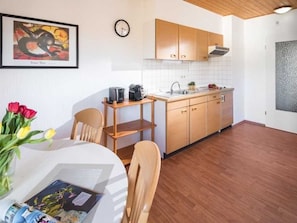 A modern kitchen with wooden cabinets, a sink, and a coffee machine. There is a dining table with chairs and a vase of flowers.