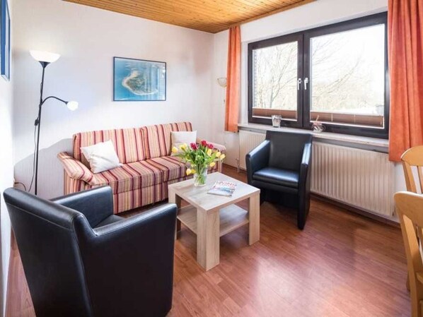 A furnished living room with a striped sofa, a coffee table, a black leather chair, and a window with curtains.
