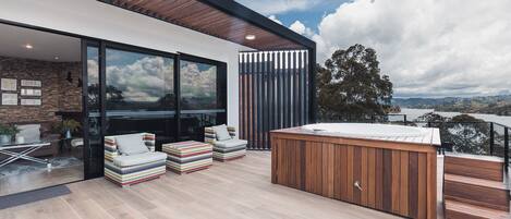 A modern outdoor living area with a hot tub, seating, and a view of the landscape.