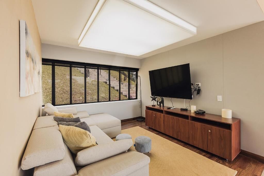 A modern living room with a large window, a flat-screen TV, and a wooden entertainment unit.