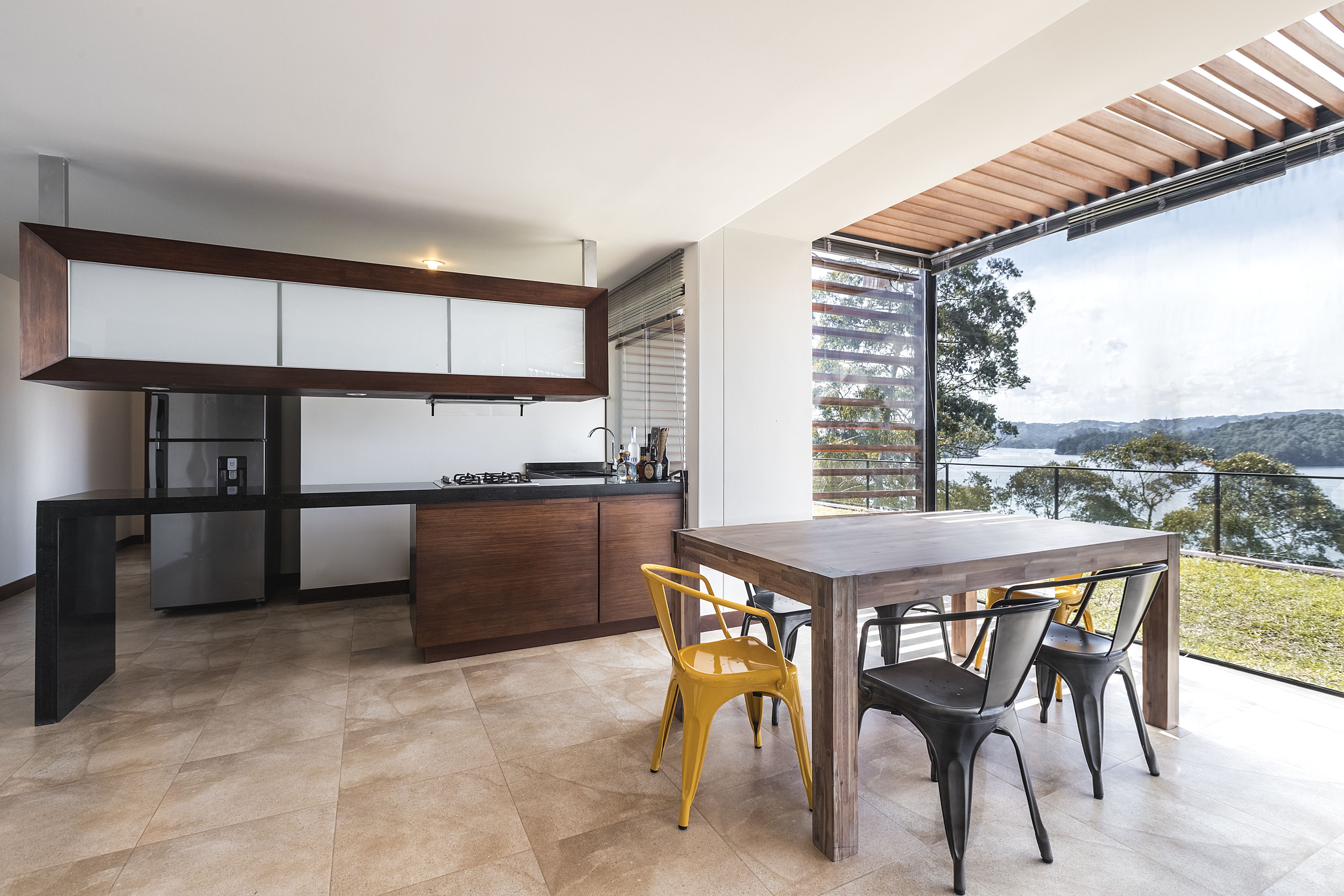 Une cuisine moderne dotée d’un grand îlot central, d’un coin repas avec une table et des chaises en bois, et offrant une vue sur un lac grâce à de grandes fenêtres.