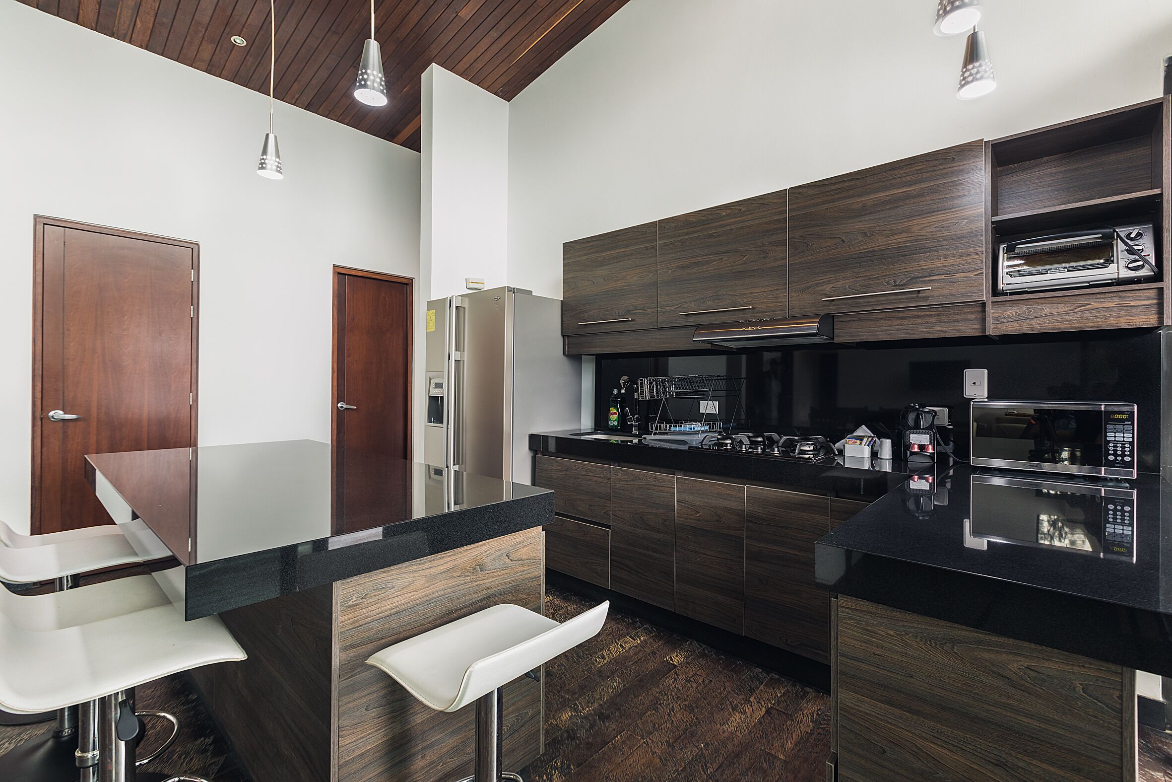 A modern kitchen with dark wood cabinets, stainless steel appliances, and a black countertop.