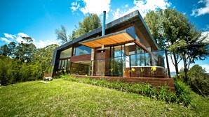 A modern house with large glass windows, a wooden deck, and a grassy yard. - Luxé Cabañas (Guatapé)