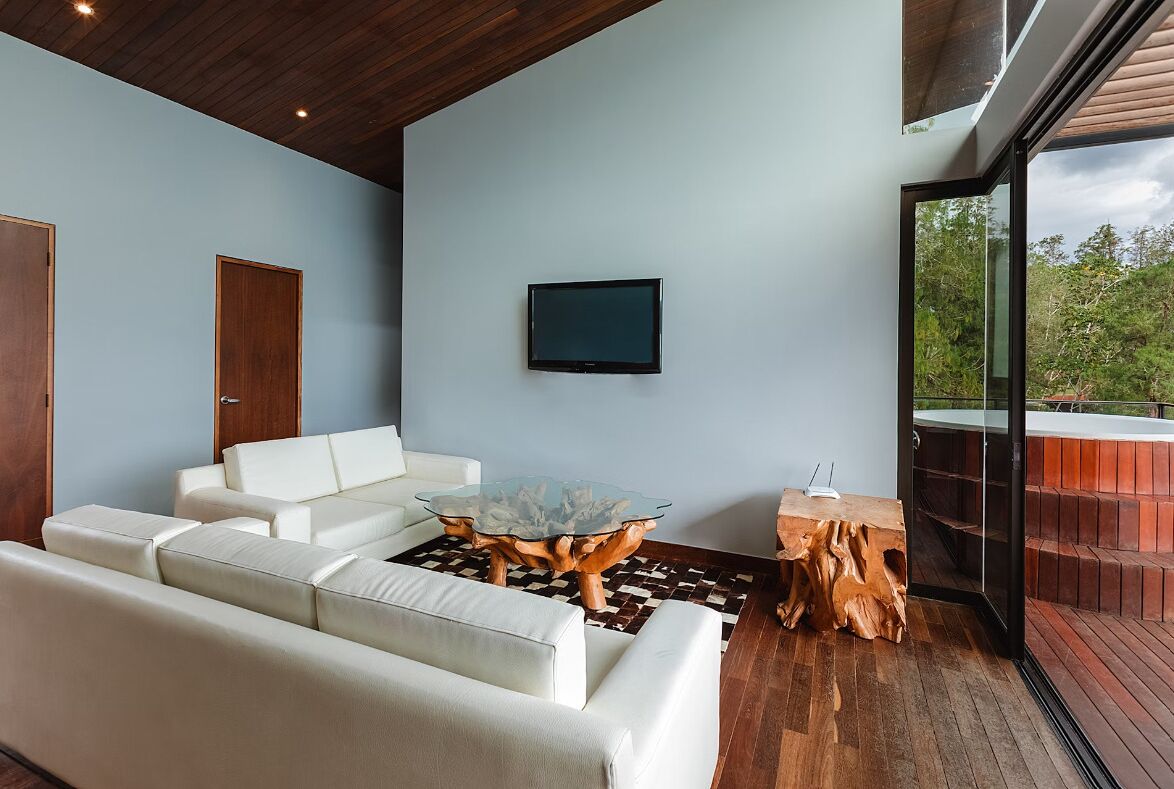 A modern living room with a glass coffee table, white sofa, and a television mounted on the wall.