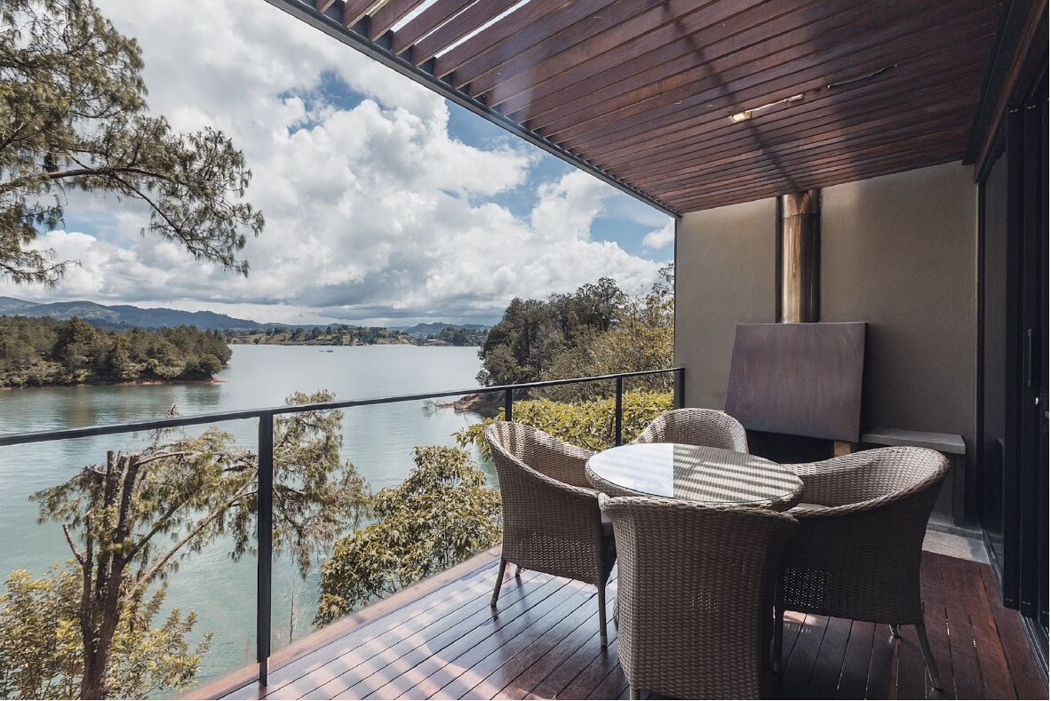 A balcony with wicker furniture overlooking a lake and mountains.