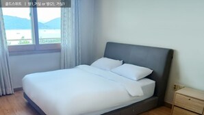 A bedroom with a bed, a nightstand, and a window with a view of a body of water and hills. - Ilsung Gyeongju Condominium Resort (Gyeongju)