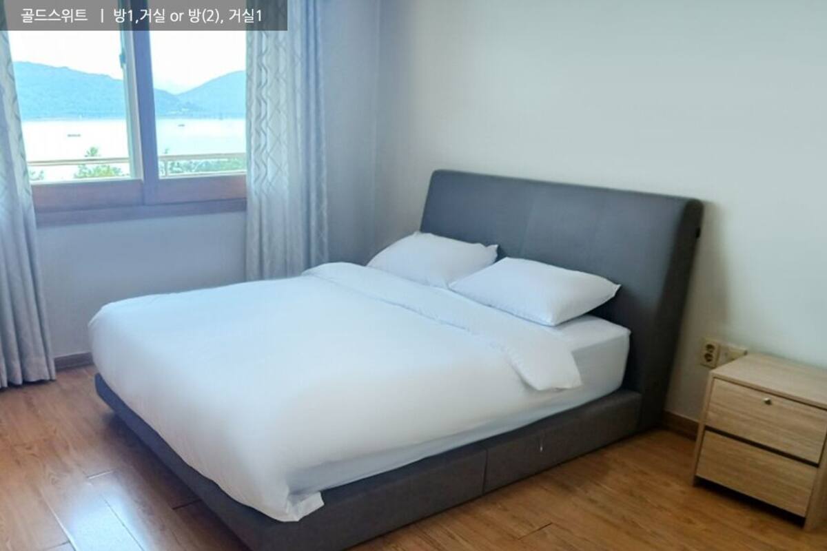A bedroom with a bed, a nightstand, and a window with a view of a body of water and hills.