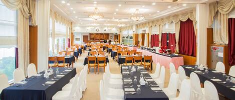 A banquet hall with multiple tables set for dining, white chairs, and chandeliers.
