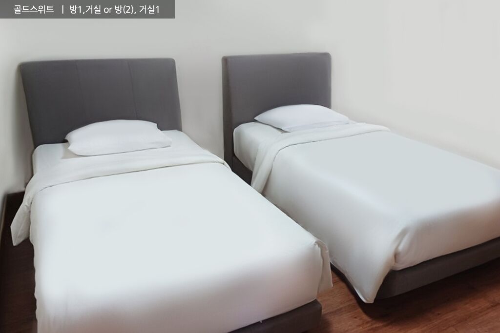 Deux lits simples avec des têtes de lit grises et du linge de lit blanc dans une chambre.