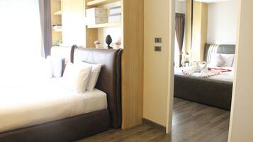 Quarto de hotel com uma cama grande, uma cama menor, piso de madeira e prateleiras embutidas com caixas de armazenamento.