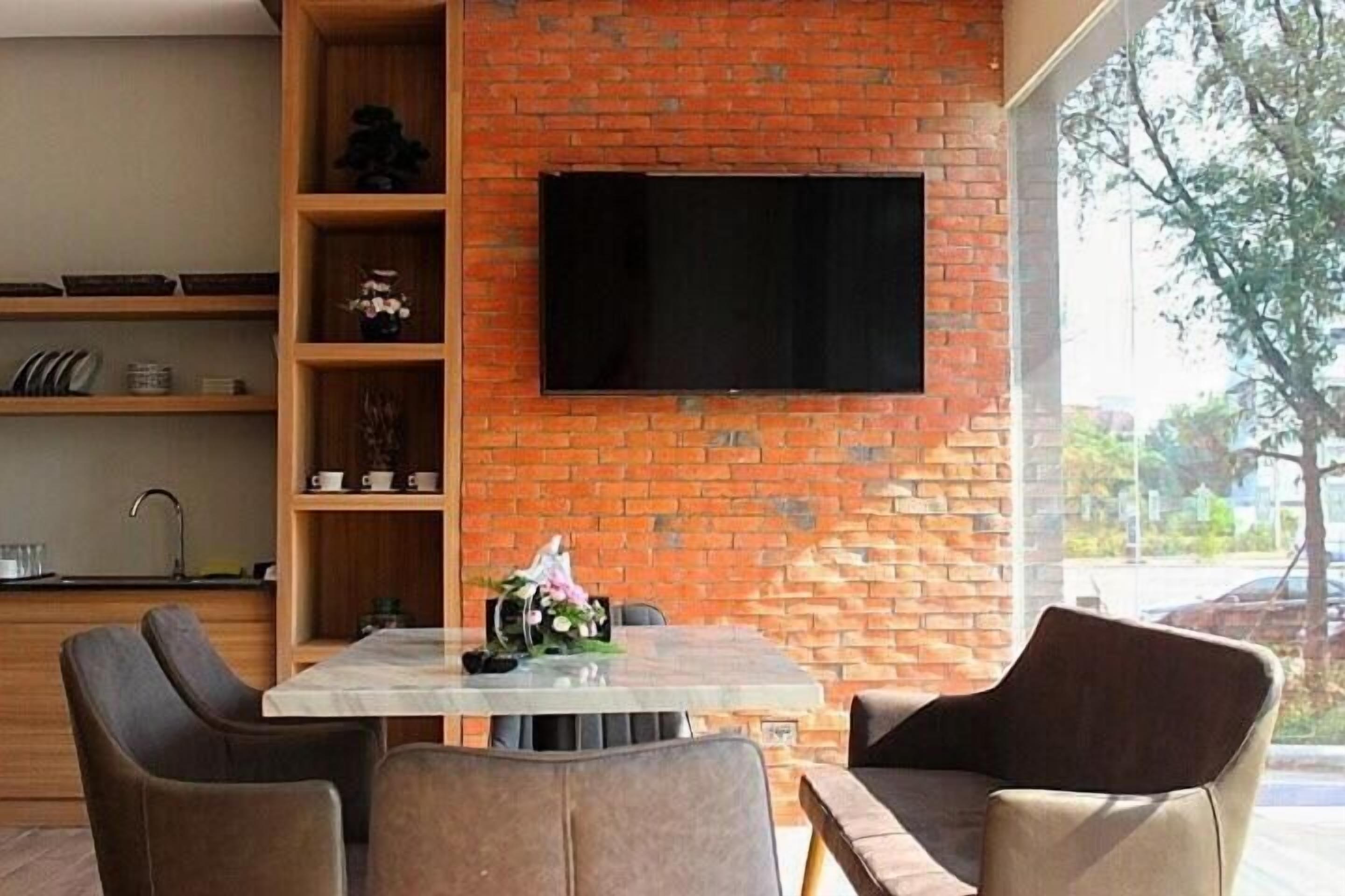 Una cocina moderna con pared de ladrillo, un televisor de pantalla plana sobre una mesa de comedor, y vista al exterior.