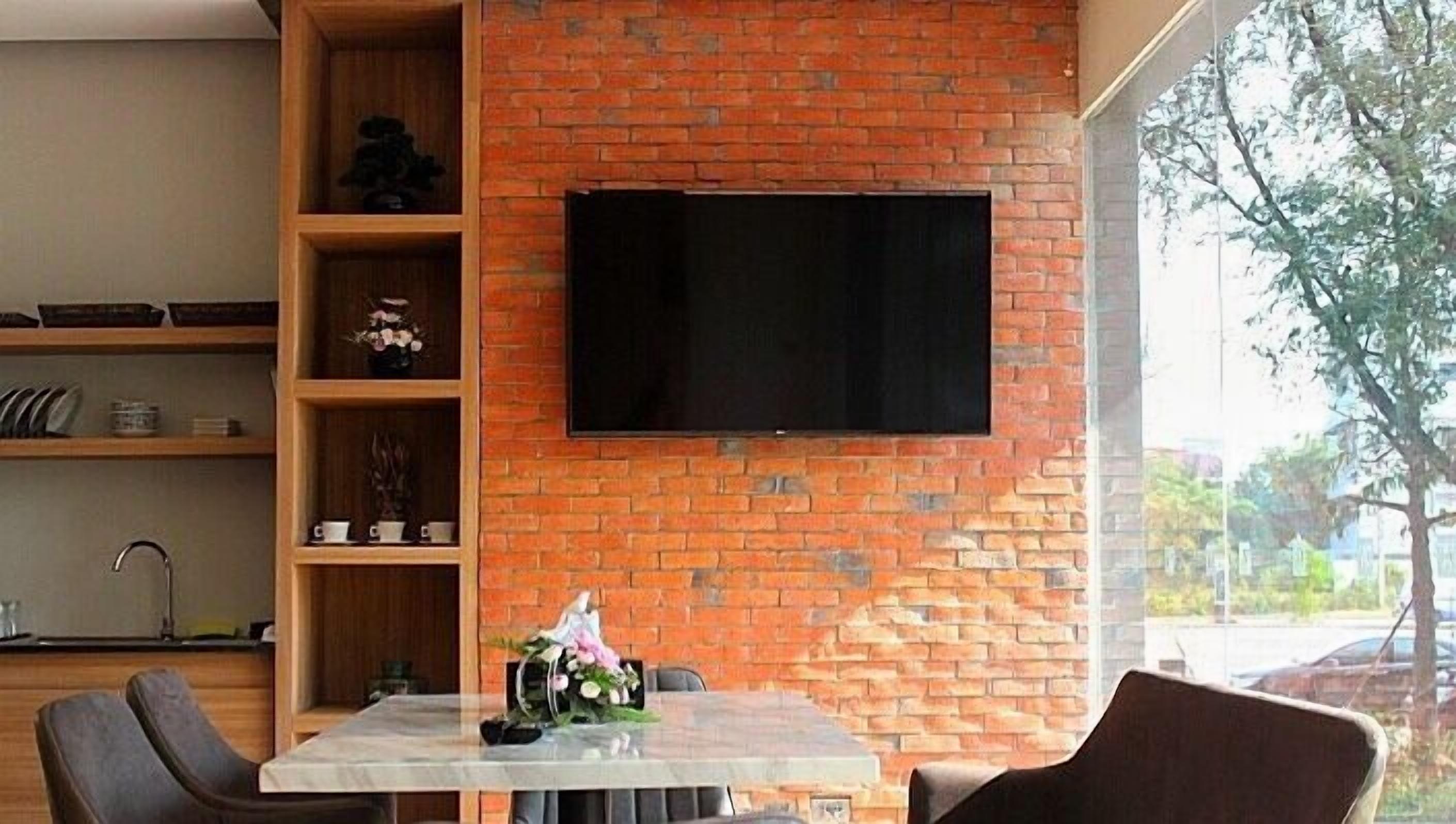 Ein modernes Wohnzimmer mit Backsteinwand, einem flachbildfernseher über einem Tisch und einem Fenster mit Blick ins Freie.