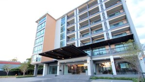 A multi-story hotel with a modern design, featuring a covered entrance and a parking area.