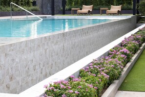 A swimming pool with a marble border, a flower bed with pink flowers, and two lounge chairs. - Wellness Chiangmai Hotel (Chiang Mai)