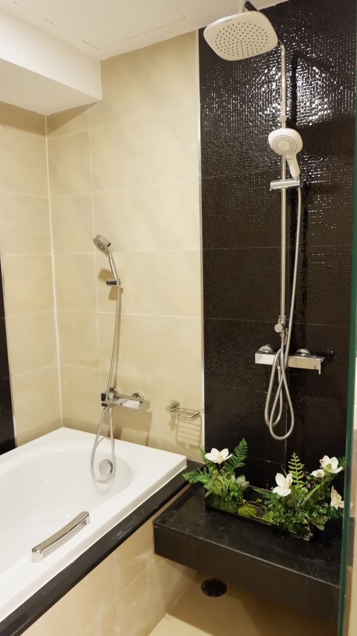 A modern bathroom with a bathtub, a shower with a rain showerhead, and a small plant on the counter.