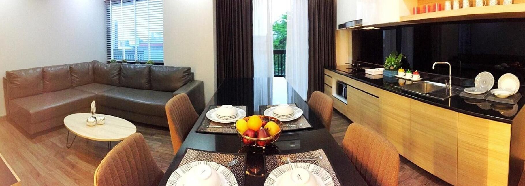 Una sala de estar moderna con un sofá, una mesa de comedor dispuesta con platos y un frutero, y una cocina con estufa y fregadero.
