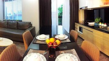 Una sala de estar moderna con un sofá, una mesa de comedor dispuesta con platos y un frutero, y una cocina con estufa y fregadero.