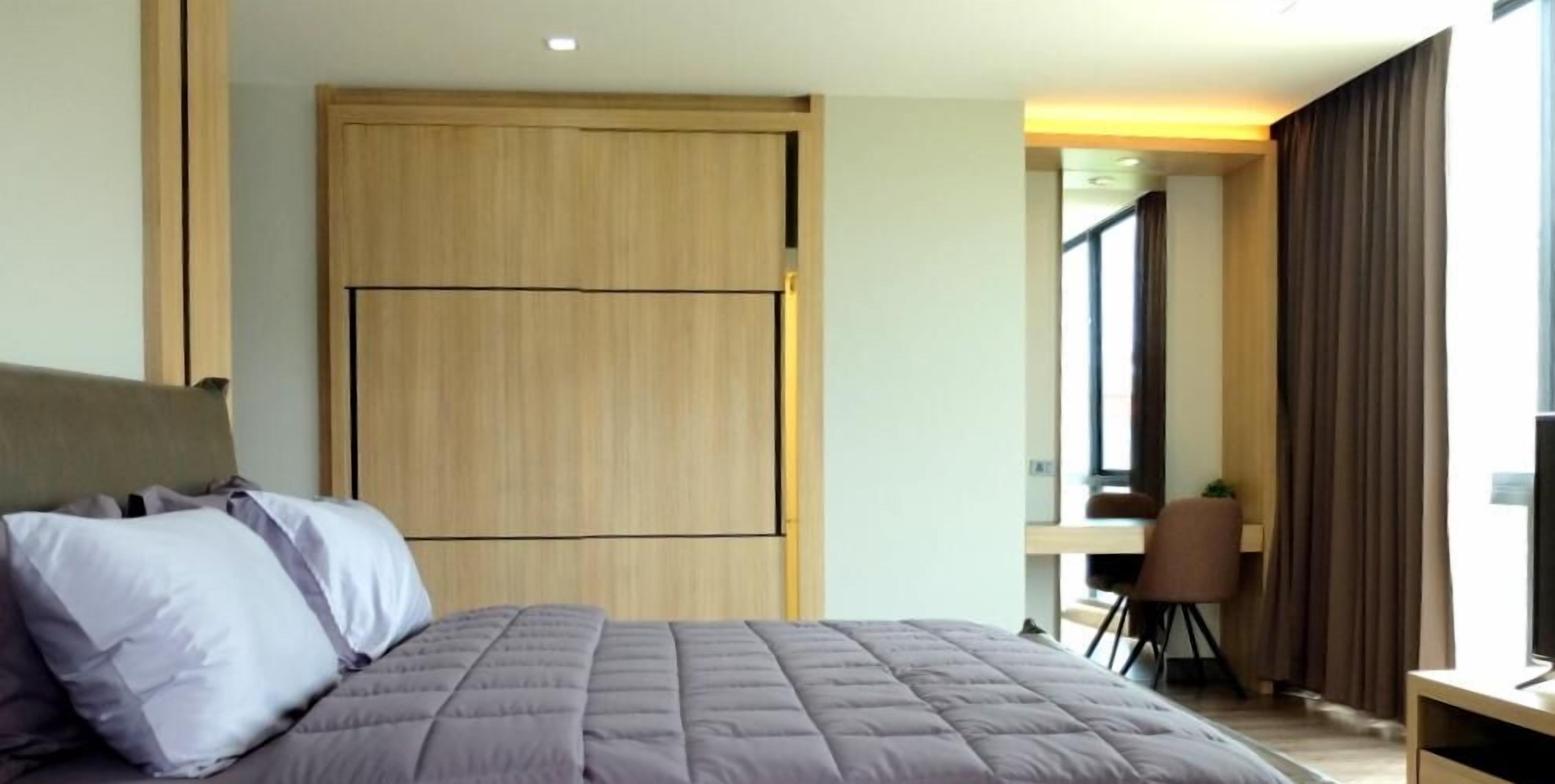 Una habitación de hotel moderna con una cama grande, un armario de madera, un escritorio y una silla.