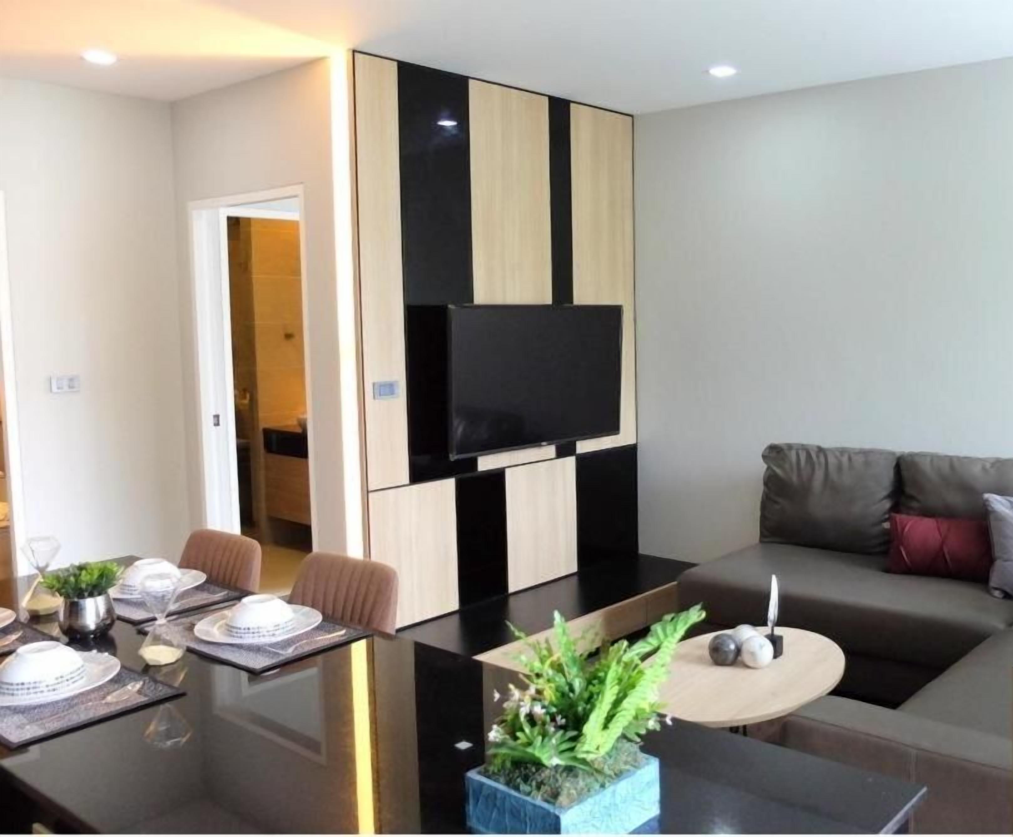 A modern living room with a sofa, a dining table set for four, and a flat-screen TV mounted on the wall.