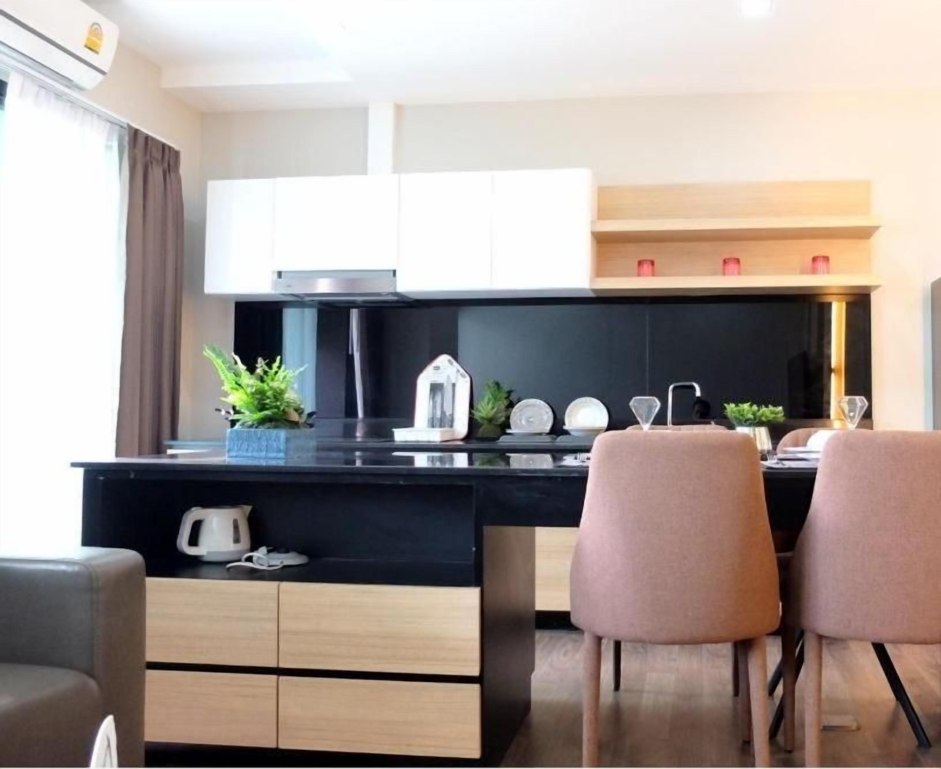 A modern kitchen with a black countertop, white cabinets, and two pink chairs.
