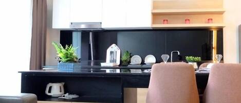 Una cocina moderna con encimera negra, armarios blancos y dos sillas rosadas.