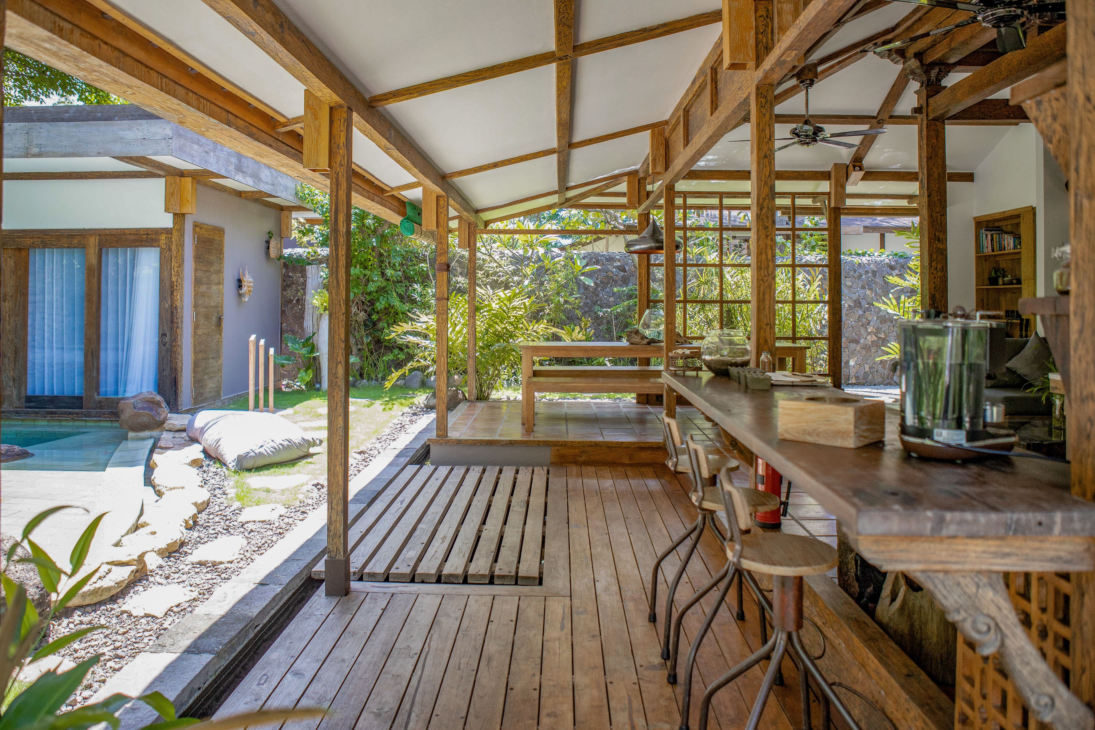 Una terraza de madera con zona de bar, piscina y vistas al jardín.