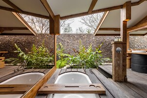 Una terraza de madera con tres tinas de hidromasaje, un muro de piedra y un banco de madera.