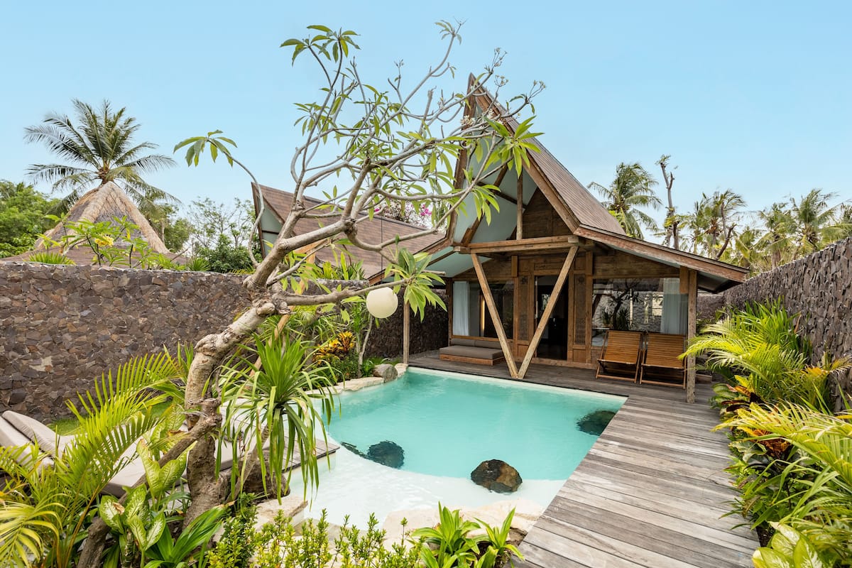 A pool area with a wooden deck, lounge chairs, and tropical plants.