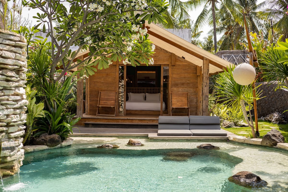 A wooden cabin with a pool, surrounded by tropical plants and rocks.
