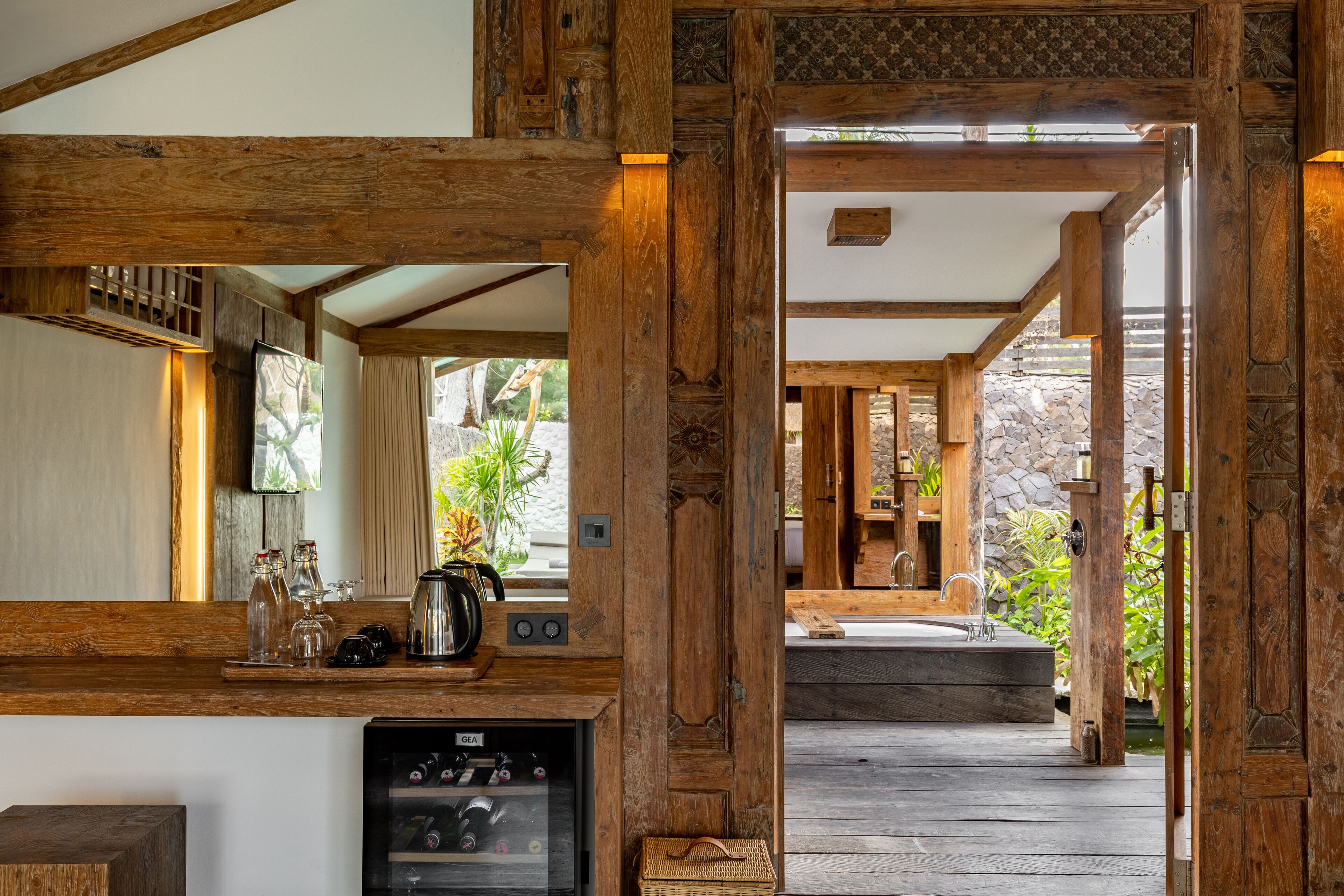 A wooden interior with a kitchen area, a stone wall, and a wooden deck leading to a bathroom.