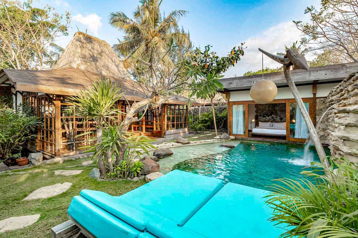A tropical resort with a swimming pool, wooden structures, and lush greenery.