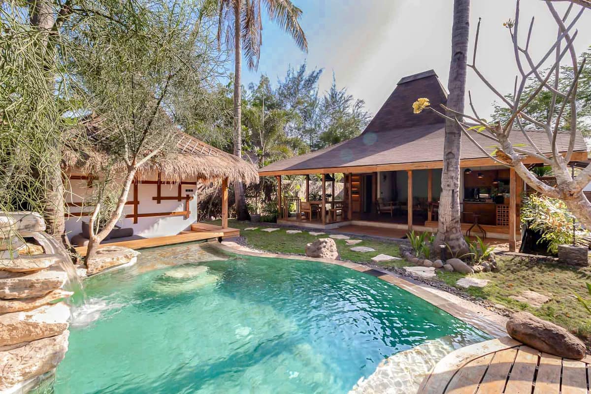 A pool area with a thatched-roof structure, a covered seating area, and a house with large windows.