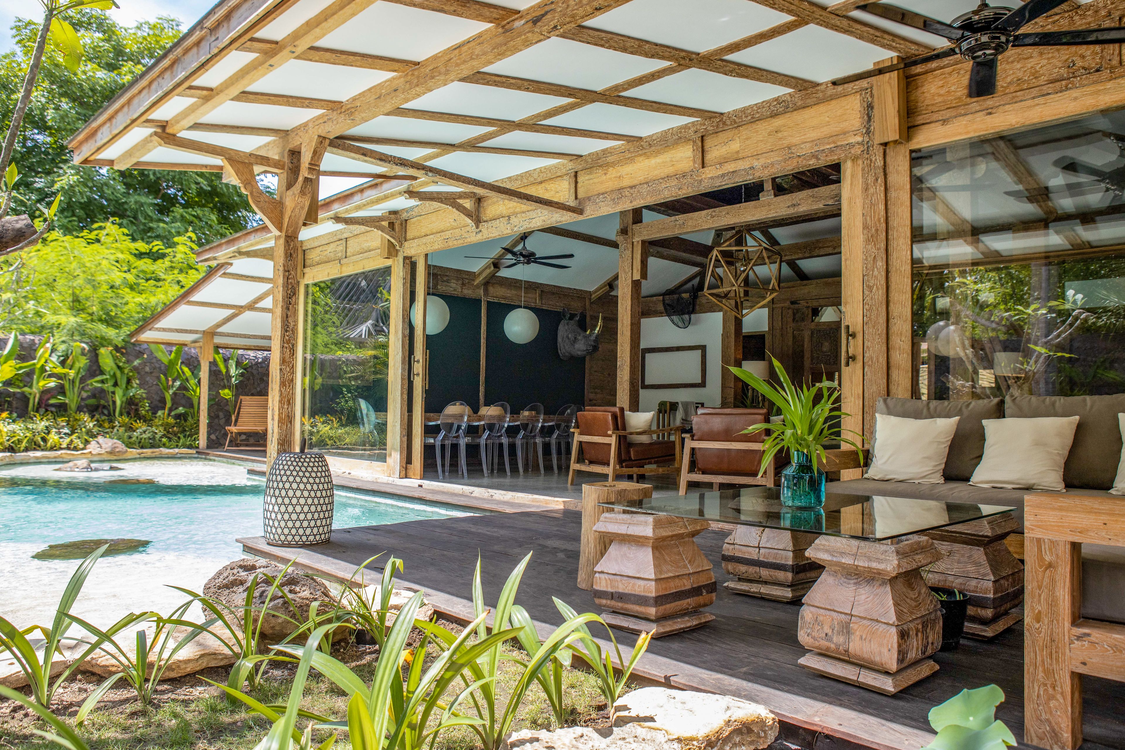 A covered outdoor area with a pool, wooden furniture, and a ceiling fan.