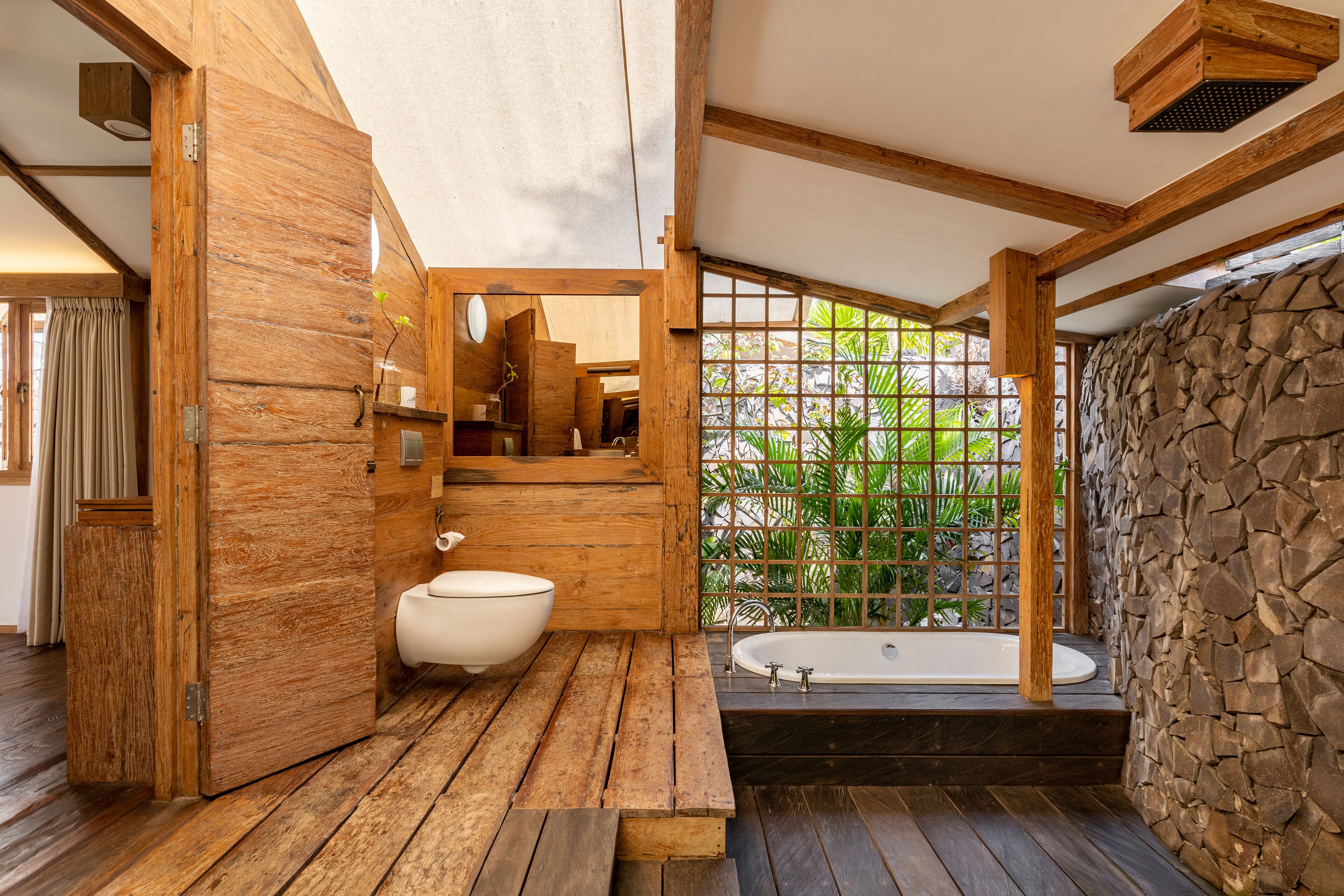 A wooden bathroom with a bathtub, a toilet, and a shower area.