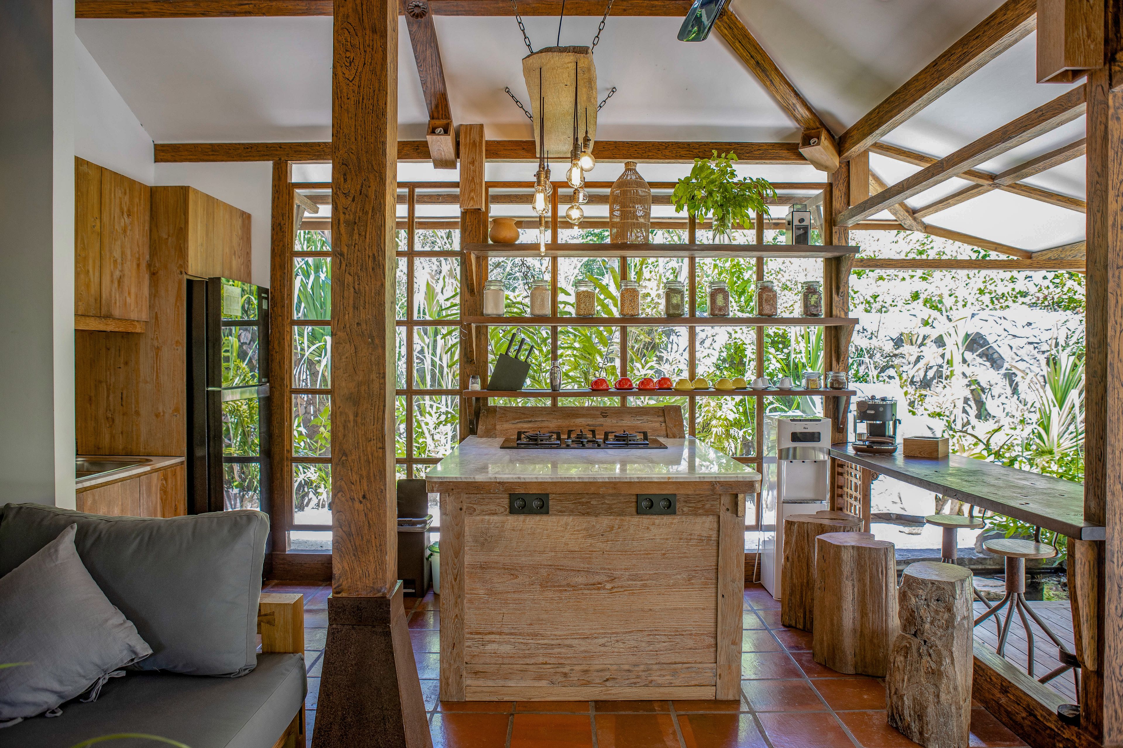 A kitchen with wooden beams, a central island, and a view of greenery through large windows.