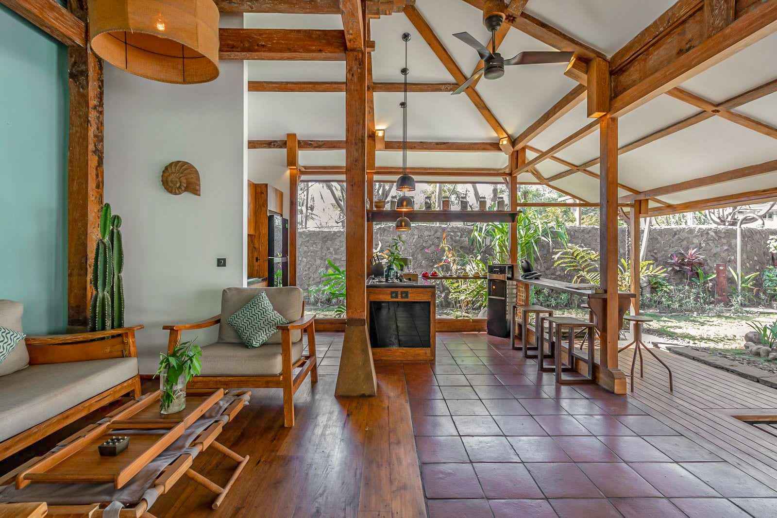 A spacious living area with wooden beams, a sofa, a dining table, and a kitchen area visible through an open archway.