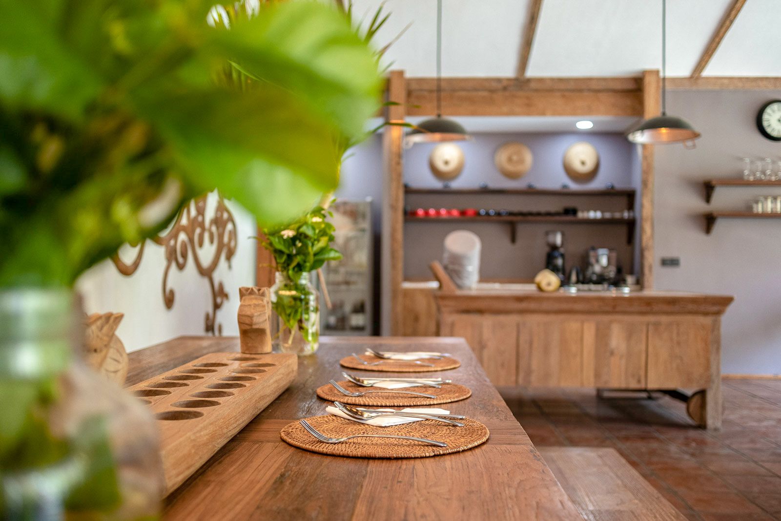 A wooden dining table set with cutlery and placemats, a wooden island with a sink, and a hanging light fixture.