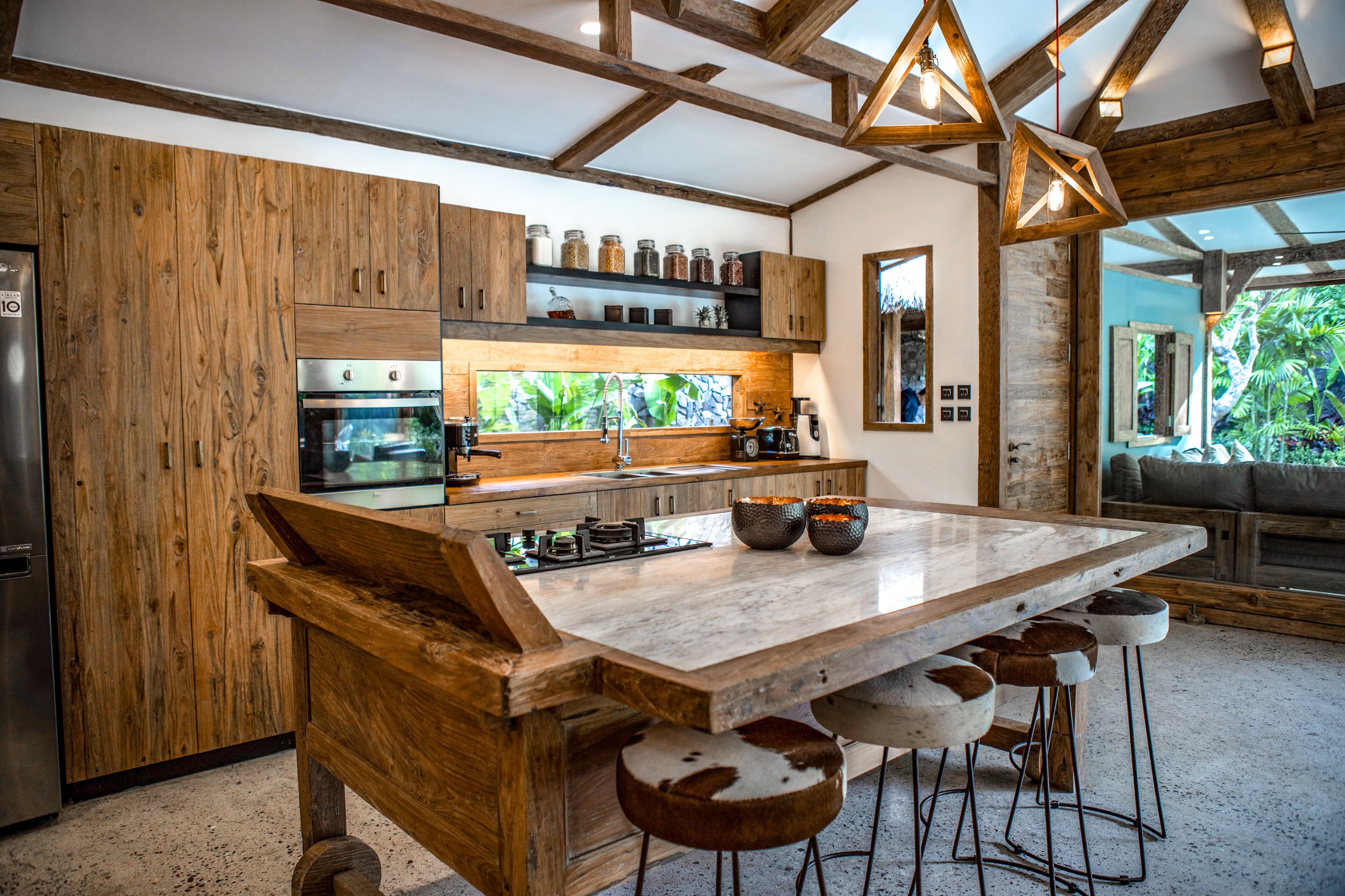 Une cuisine moderne avec des meubles en bois, un grand îlot central doté de tabourets et une vue sur la verdure à l’extérieur.
