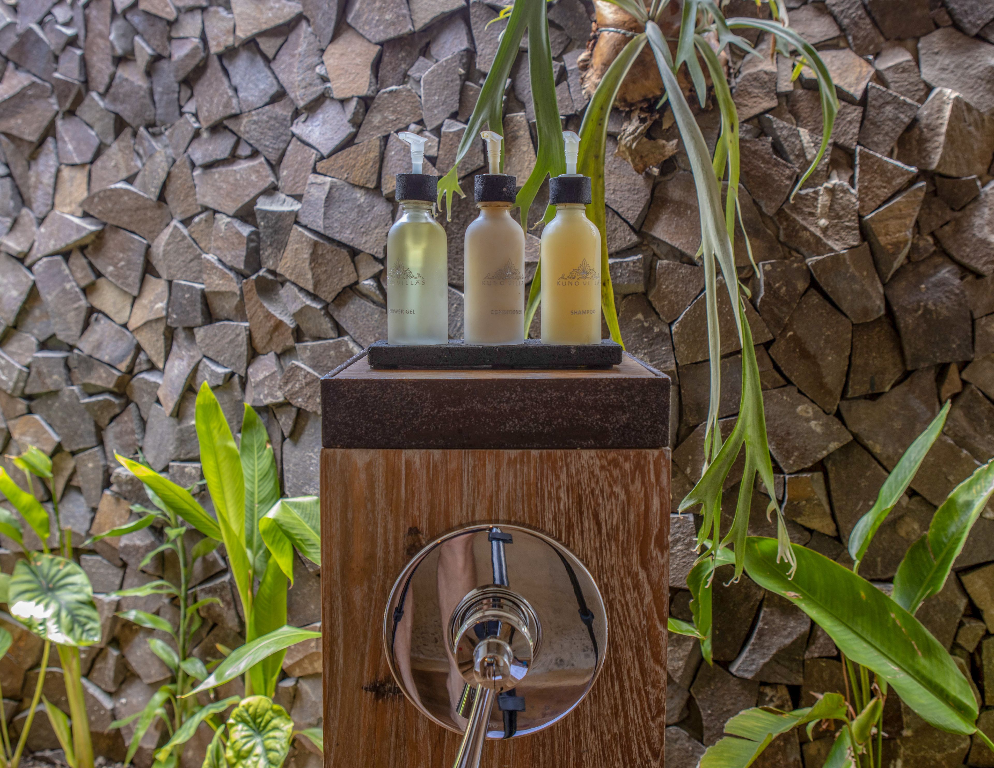 Un distributeur en bois contenant trois flacons de liquide, vraisemblablement des produits de toilette, est placé contre un mur de pierre.